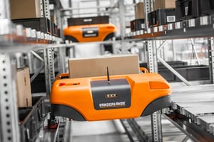 Automated shuttle robot transporting a cardboard box in a warehouse storage system.
