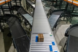 Automated warehouse conveyor system with a cardboard box moving through a sorting facility.