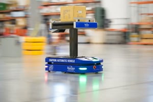 Automated guided vehicle transports a package across a warehouse floor.