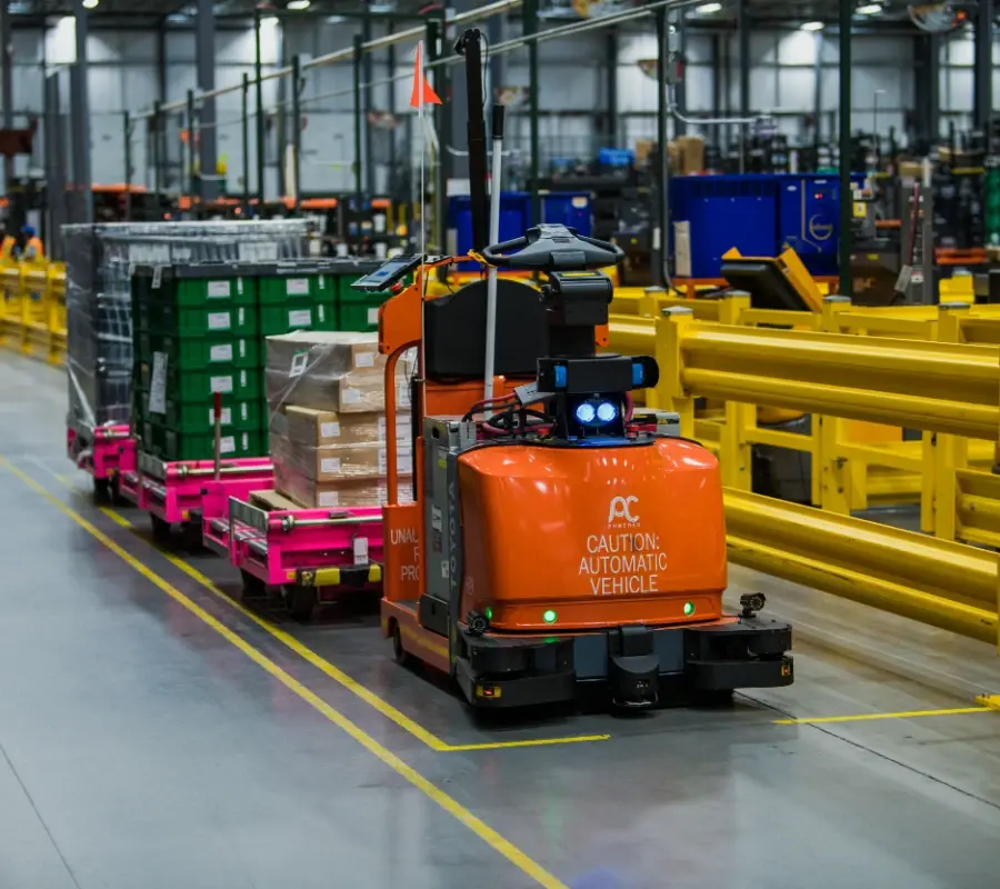 Toyota automated warehouse vehicle towing carts of inventory through a large distribution center.