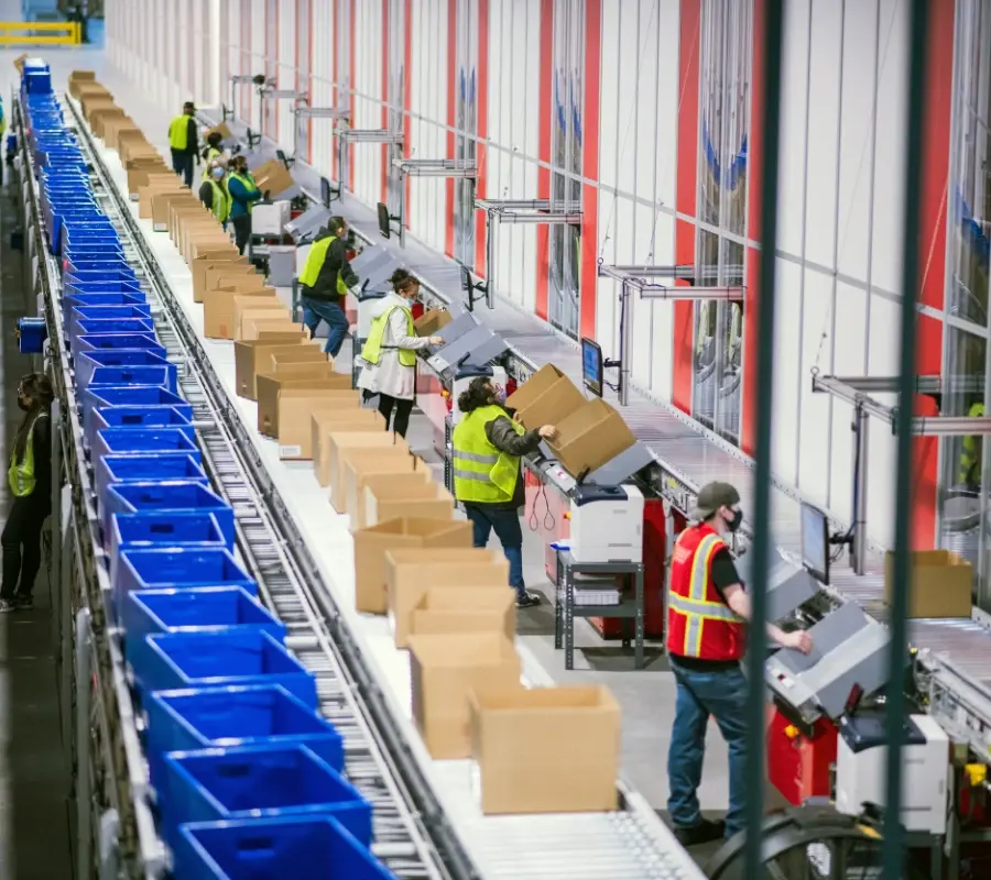 Warehouse workers processing apparel orders next to conveyor belt system in a fulfillment center.
