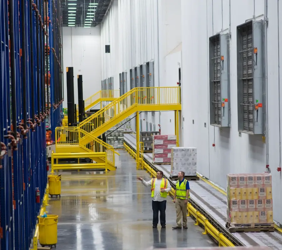 Customer walking through a large grocery distribution warehouse with high-density storage racks.