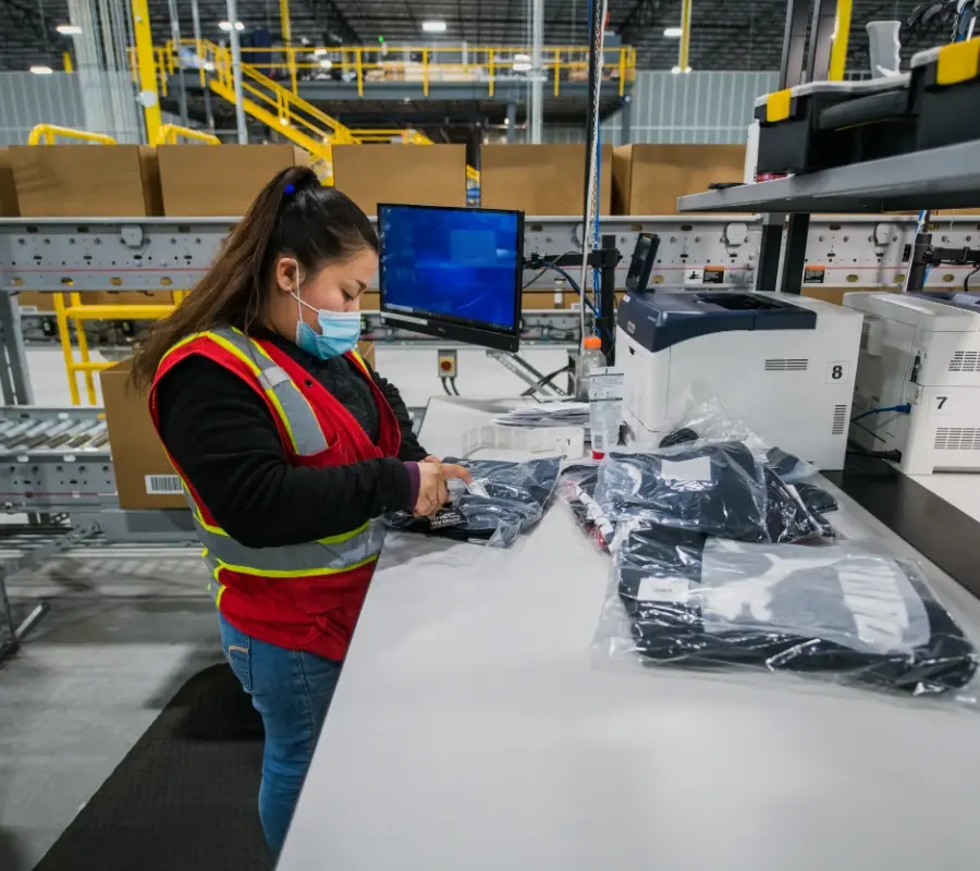 A warehouse worker packages apparel items at a fulfillment center workstation.