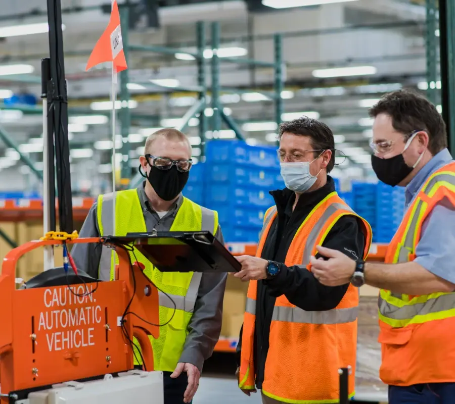 Three specialists providing warehouse automation support near an automated vehicle