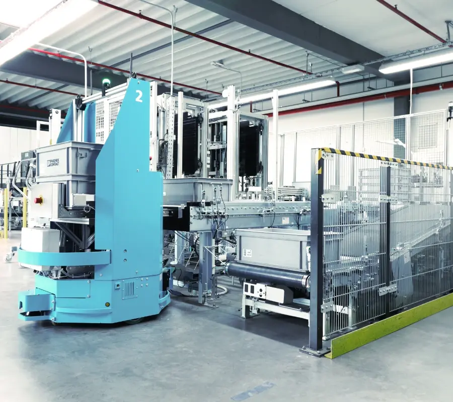 A blue automated guided vehicle (AGV) interfaces with a conveyor system in a modern industrial facility.