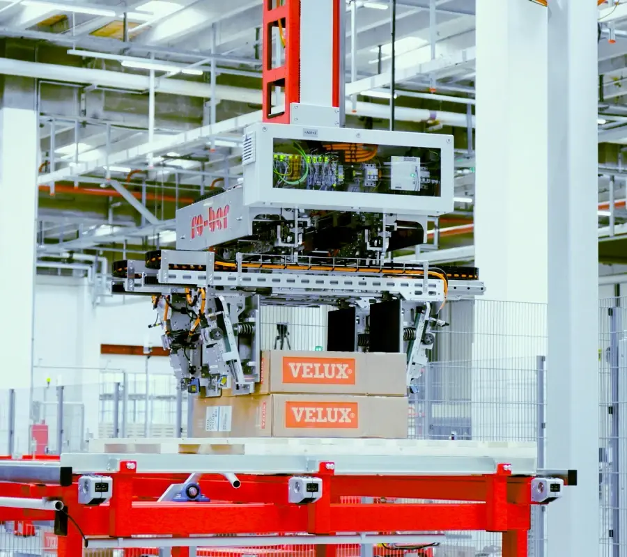 An automated palletizing robot lifting Velux boxes in a high-tech warehouse facility.