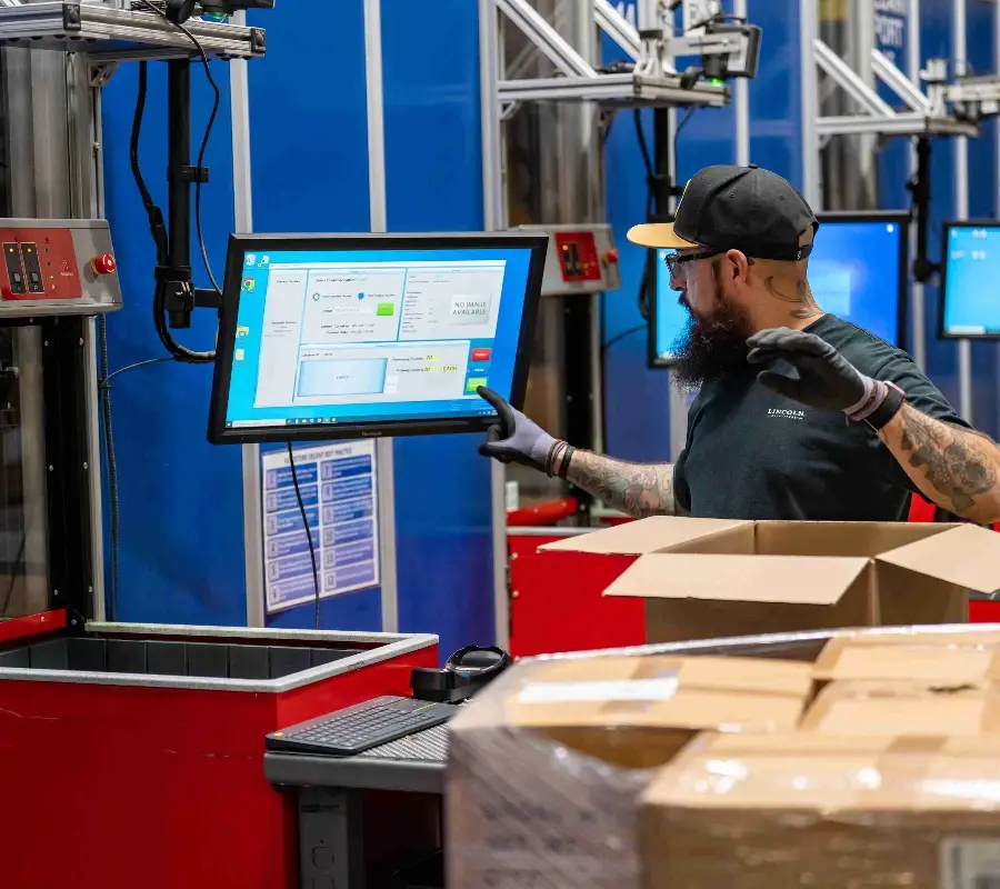 Warehouse worker using a touchscreen at a goods-to-person workstation for automated order fulfillment.