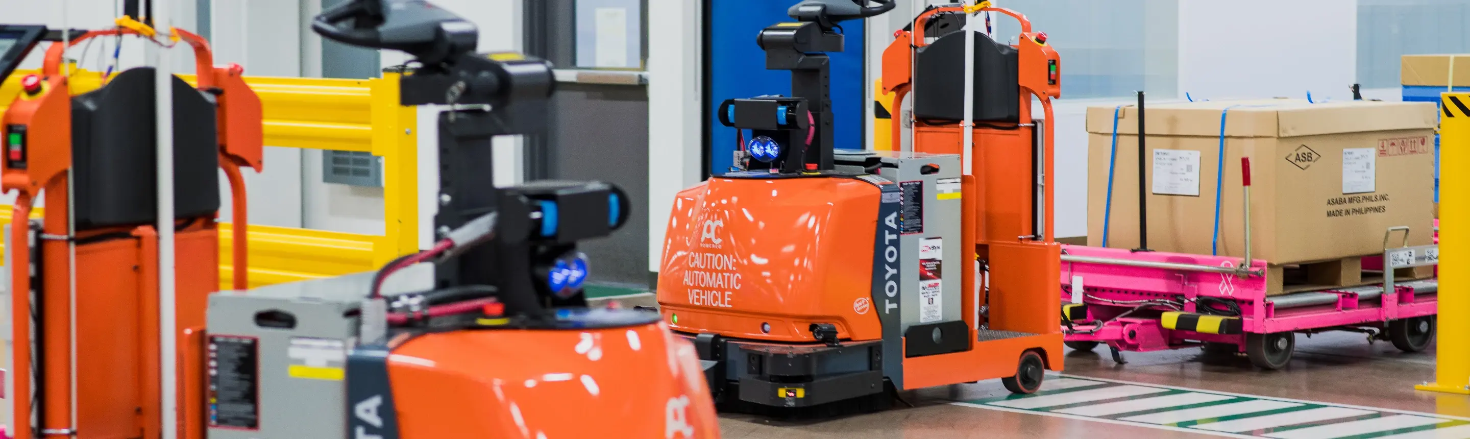Orange Toyota automated guided vehicles (AGVs) transporting goods in a clean warehouse facility.