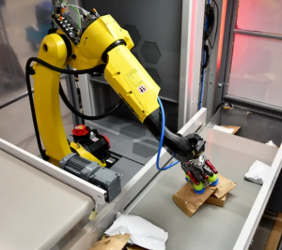 A yellow piece-picking robot arm sorts brown paper packages on an automated conveyor system.